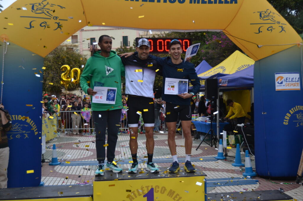 Tres corredores en el podio de la San Silvestre de Melilla con medallas y diplomas.