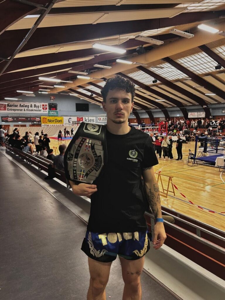Joven deportista del Club Olympic Center Melilla sosteniendo un cinturón de campeón en un evento de kickboxing.