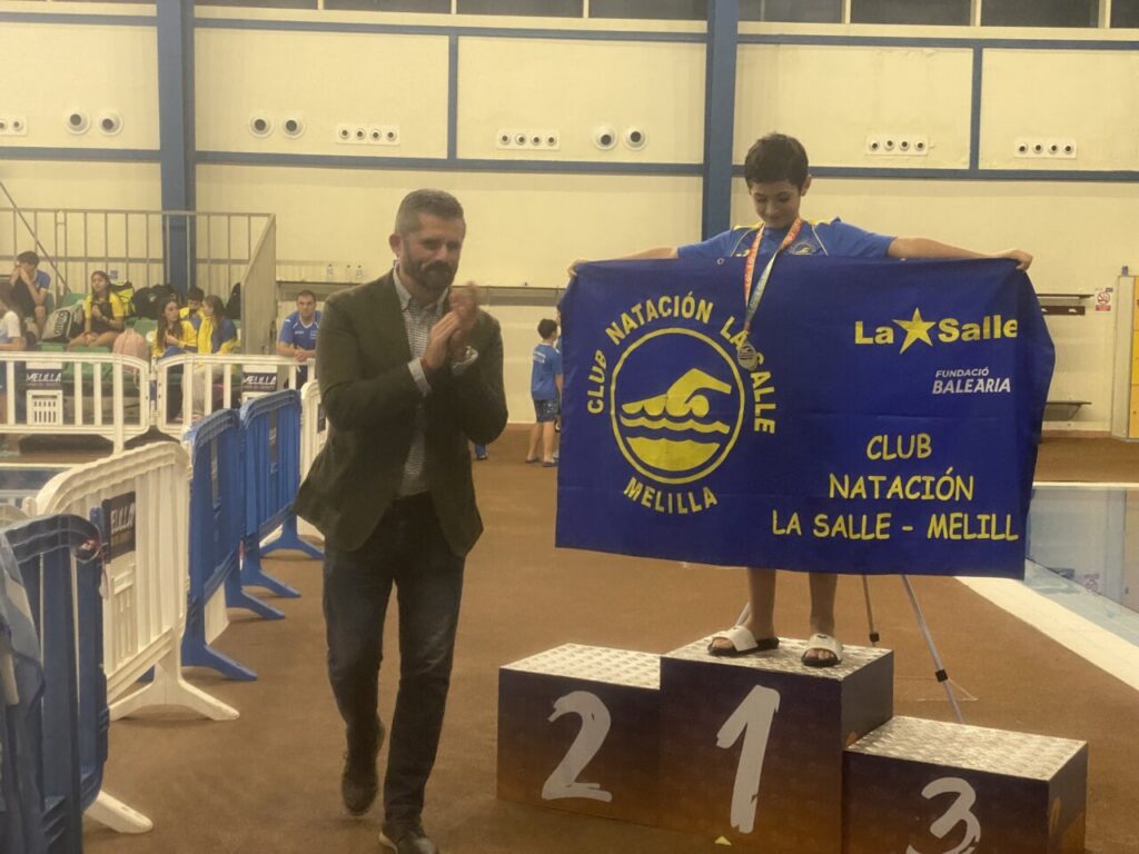 Niño sosteniendo una bandera del Club Natación La Salle en el podio