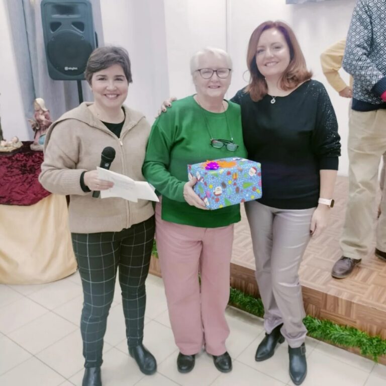Tres mujeres sonrientes en un evento de repostería con un regalo colorido