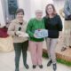 Tres mujeres sonrientes en un evento de repostería con un regalo colorido