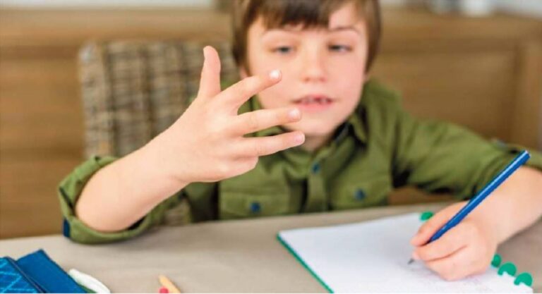 Niño contando con los dedos mientras escribe en una libreta