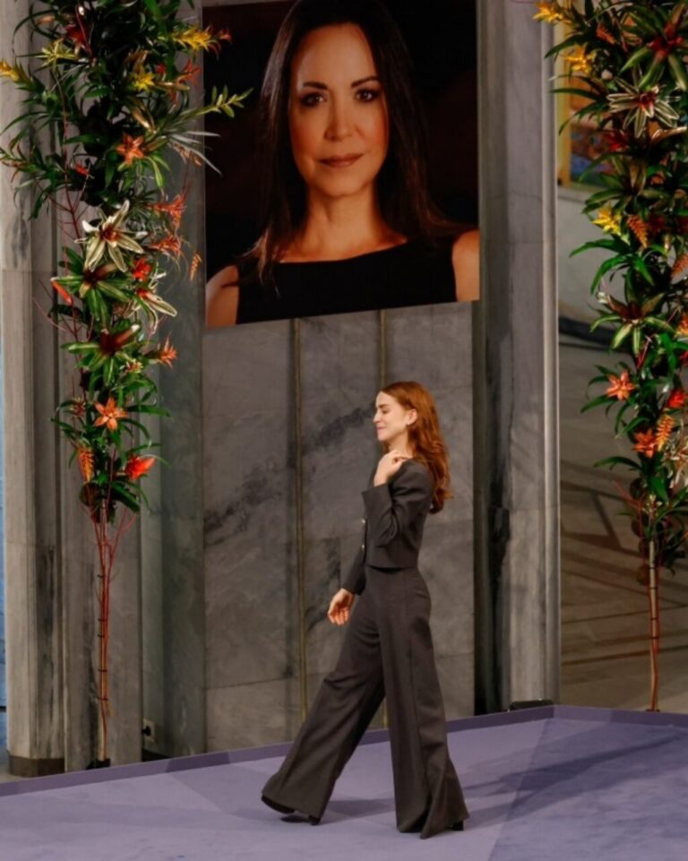 María Corina Machado en un evento con un retrato de fondo