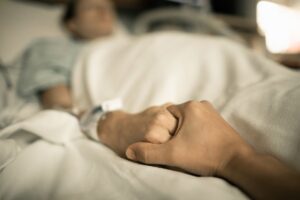 Persona sosteniendo la mano de un paciente en una cama de hospital