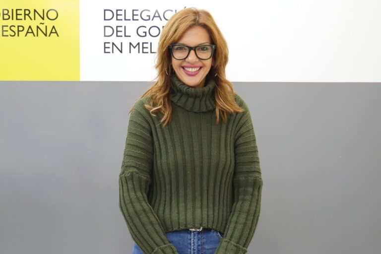 Persona sonriente con suéter verde en un evento gubernamental en Melilla