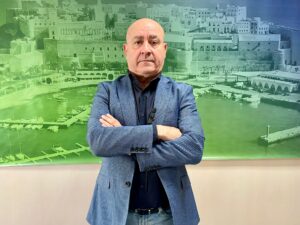 Hombre de pie con brazos cruzados frente a un fondo de puerto