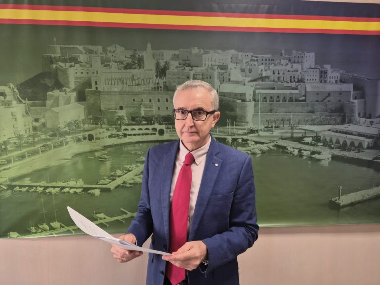 Persona sosteniendo documentos frente a un fondo histórico de una ciudad costera