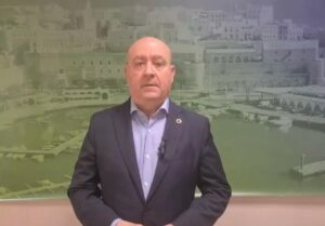 Hombre de pie frente a un paisaje marino con edificios.