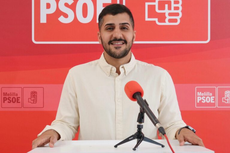 Persona sonriendo frente a un fondo rojo con el logo del PSOE