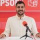 Persona sonriendo frente a un fondo rojo con el logo del PSOE
