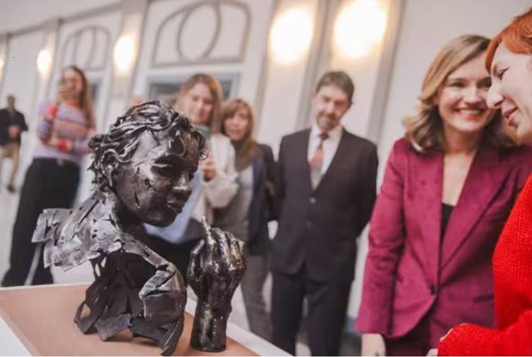 Escultura de un niño en una exposición con personas observando.