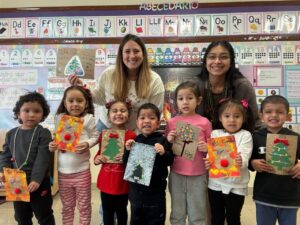 Niños mostrando tarjetas navideñas en un aula con sus maestras.
