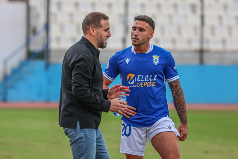 Javi Motos conversando con un jugador de la U.D. Melilla en el campo