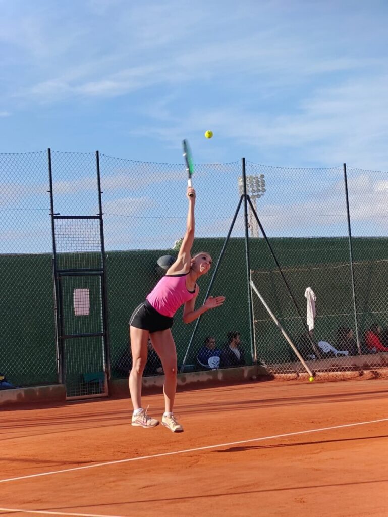 Jugadora de tenis realizando un saque en una cancha de tierra batida