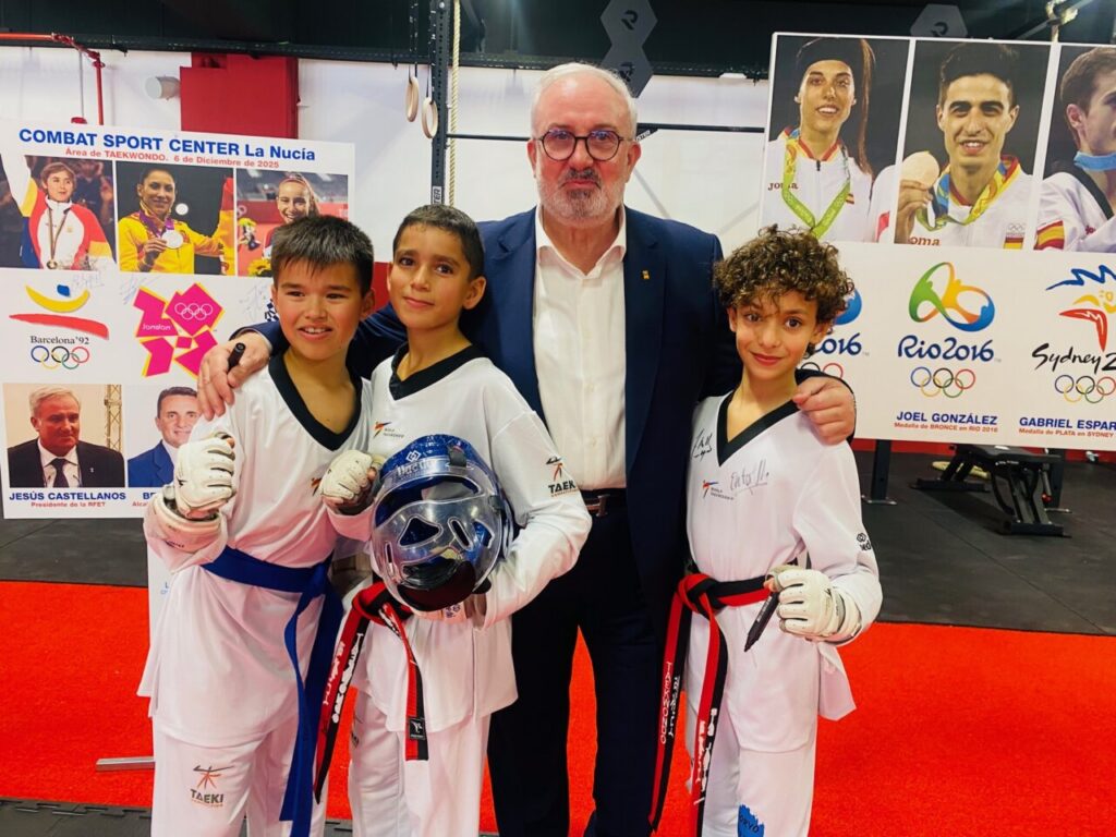 Tres jóvenes taekwondistas posando con un adulto en un evento deportivo