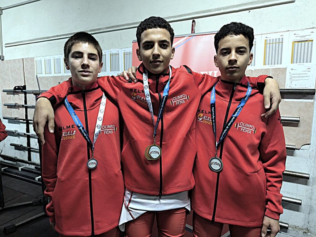 Tres jóvenes medallistas del club Olimpo Fénix en sus chaquetas rojas