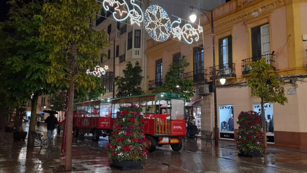 Calle iluminada con decoraciones navideñas y un tranvía rojo