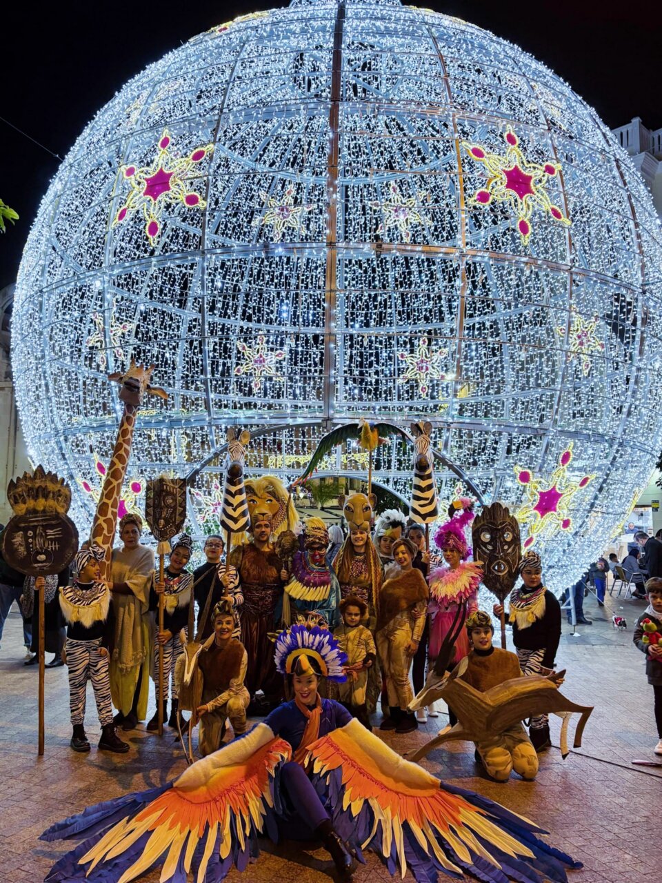 Grupo de personas disfrazadas en el pasacalles 'Dibulandia' con decoraciones luminosas.