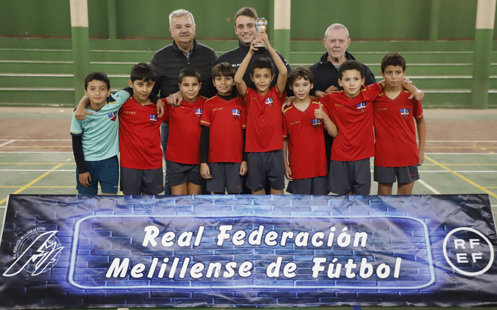 Equipo de fútbol benjamín con trofeo en la pista polideportiva