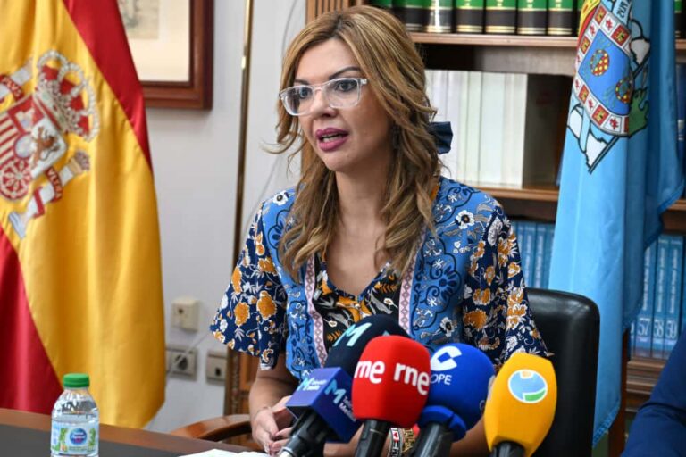 Mujer en rueda de prensa con micrófonos y banderas de fondo