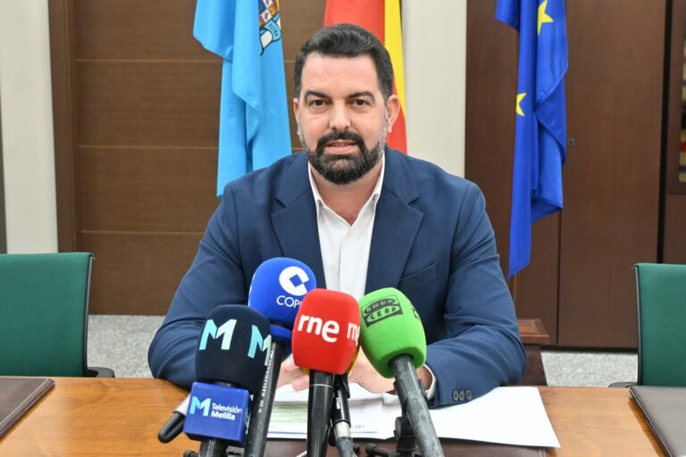 Hombre en rueda de prensa con micrófonos y banderas de fondo