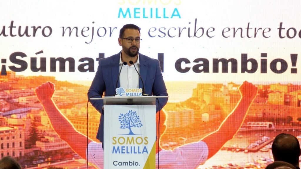 Miembro de Somos Melilla hablando en un evento ante un público numeroso.