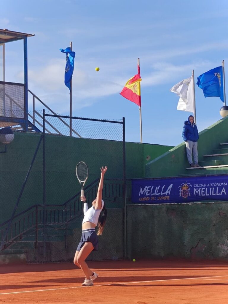 Jugadora de tenis lanzando la pelota al aire en la cancha.