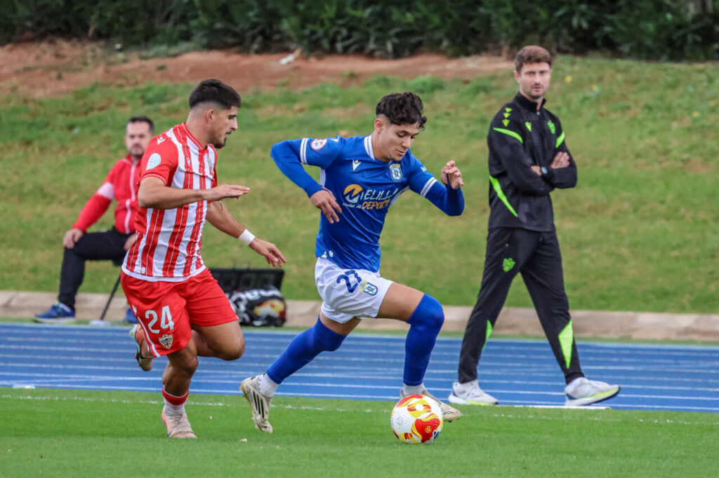 Jugador de la U.D. Melilla corriendo con el balón en un partido de fútbol
