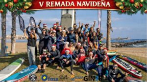 Grupo de personas en la playa celebrando la V Remada Navideña con trajes de surf y gorros navideños.
