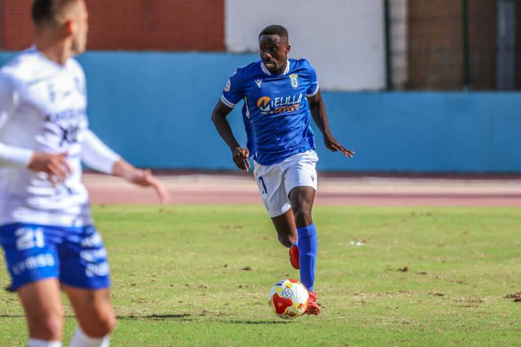 Jugador de la U.D. Melilla corriendo con el balón durante un partido de fútbol
