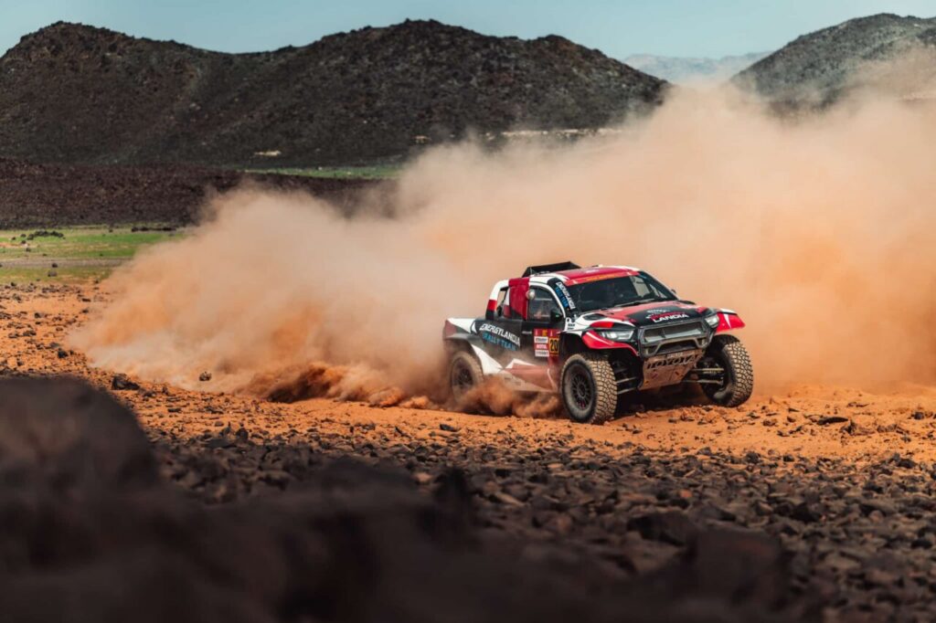 Coche de rally atravesando un terreno polvoriento en Al-Ula