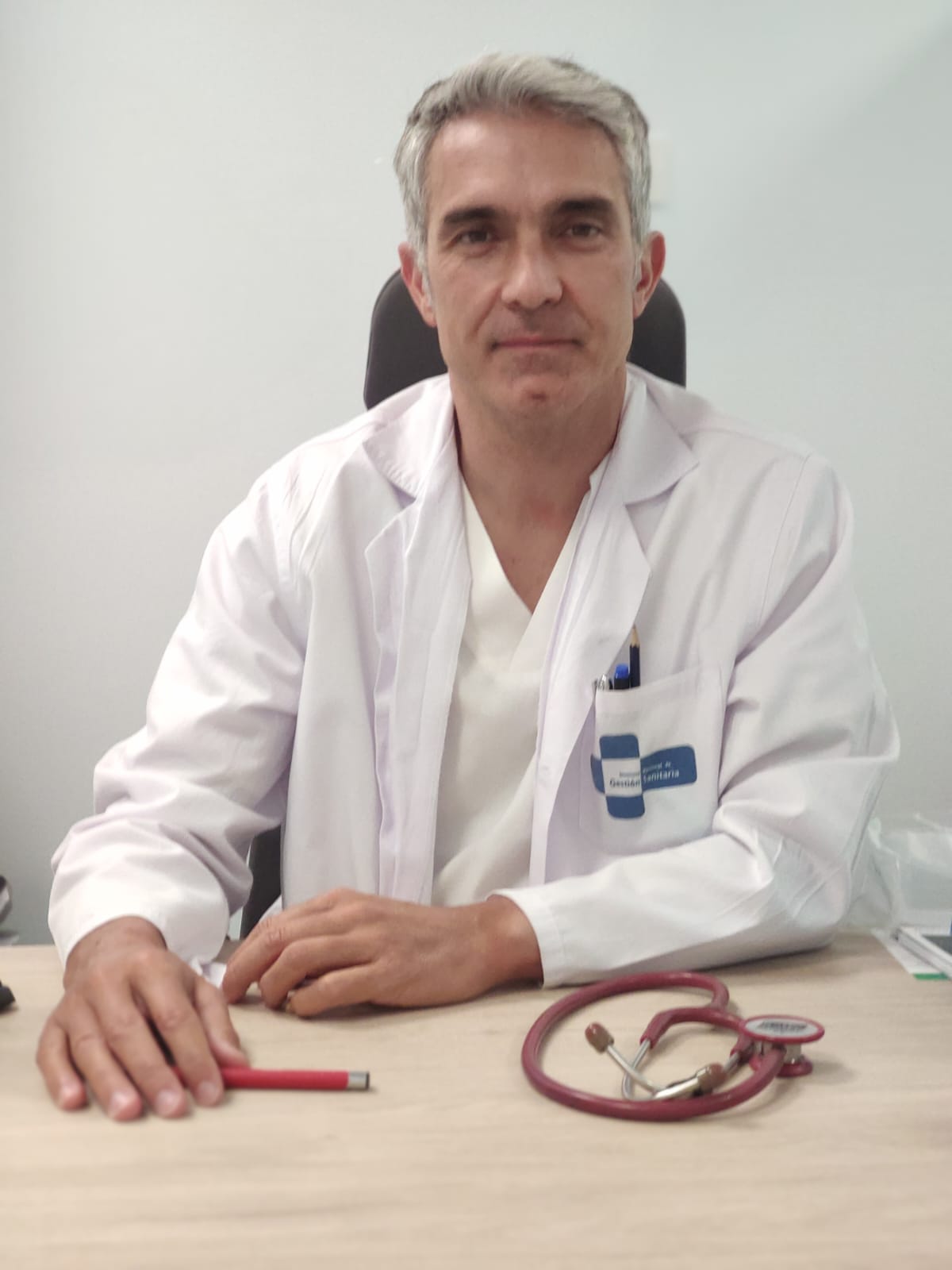 Médico en bata blanca sentado en su consulta con estetoscopio
