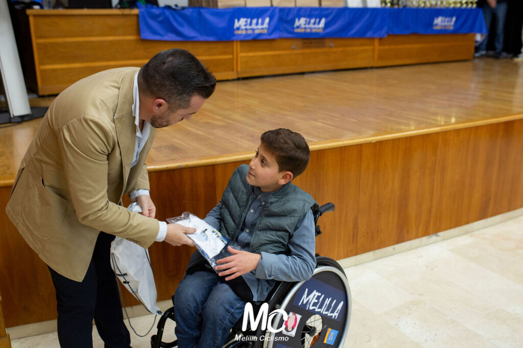 Un niño en silla de ruedas recibe un maillot en un evento de ciclismo.