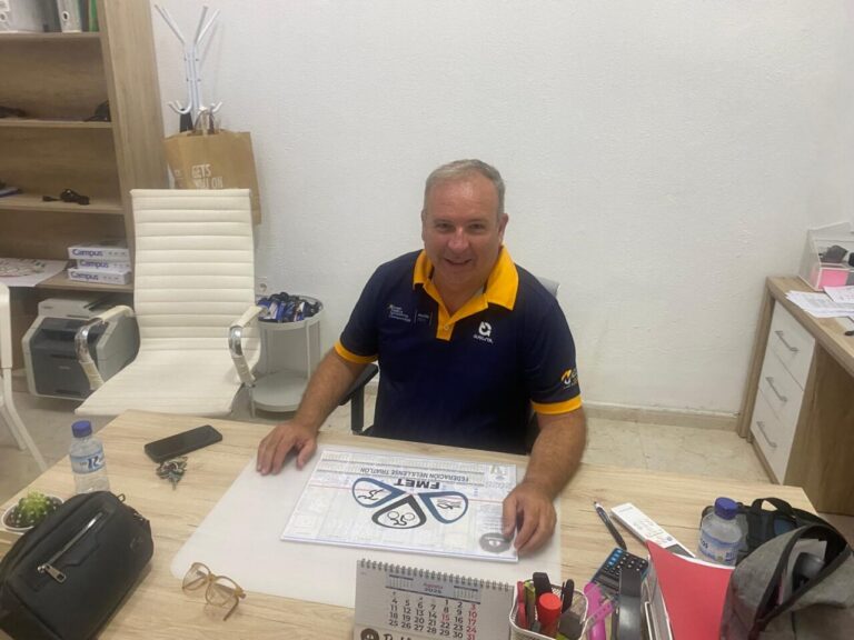 Hombre sonriente en una oficina con documentos de triatlón