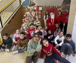 Niños y niñas en el campamento de Navidad del CEIP Velázquez con Santa Claus y árbol decorado.