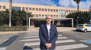 Hombre de pie frente al Hospital Comarcal con palmeras al fondo