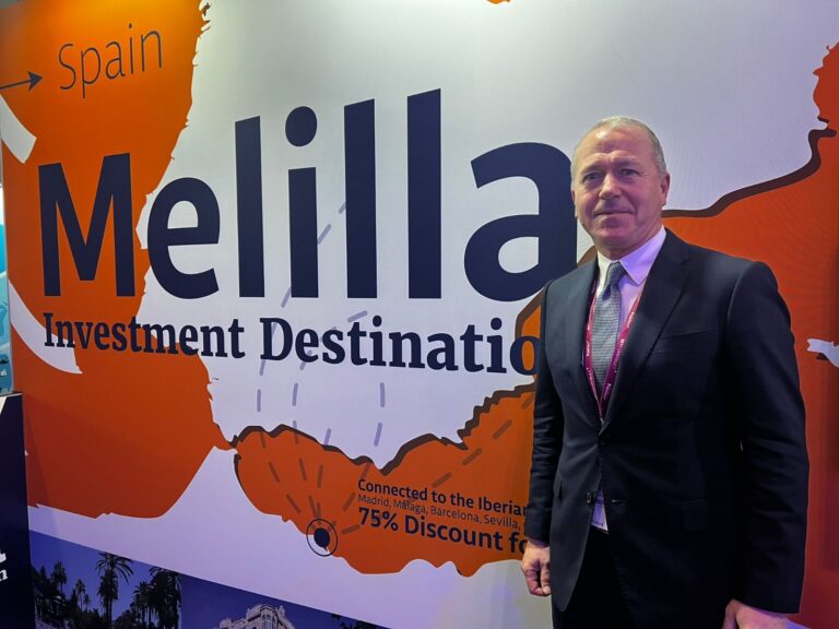 Hombre de pie junto a un cartel de Melilla como destino de inversión