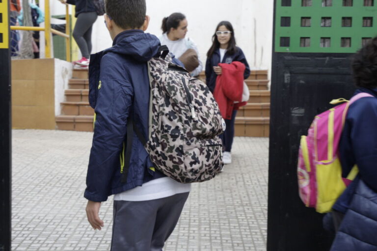 Niño con mochila camina hacia la entrada de la escuela.