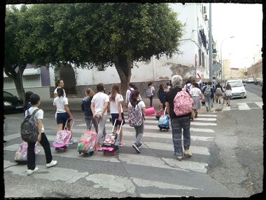 Grupo de niños cruzando la calle con maletas de colores
