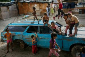 Niños jugando sobre un auto abandonado en un barrio de Venezuela