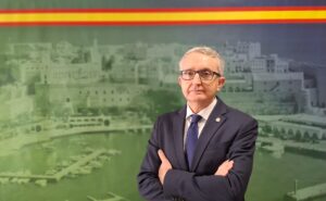Retrato de un hombre con gafas y traje frente a un fondo de Melilla.