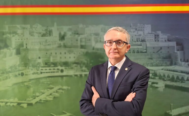 Retrato de un hombre con gafas y traje frente a un fondo de Melilla.