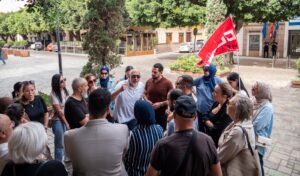 Grupo de personas reunidas en la calle con una bandera roja.