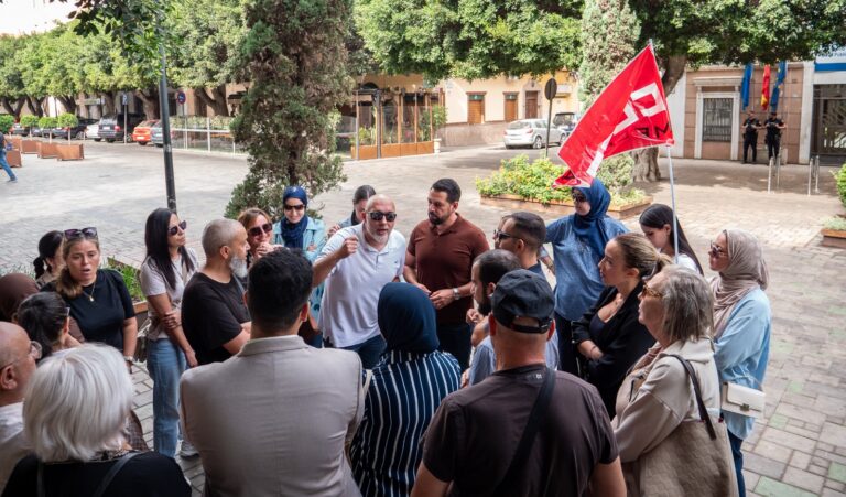 Grupo de personas reunidas en la calle con una bandera roja.