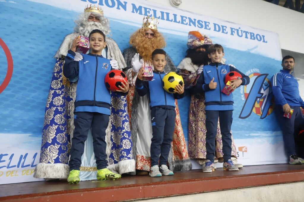 Niños posando con los Reyes Magos y regalos en un evento deportivo