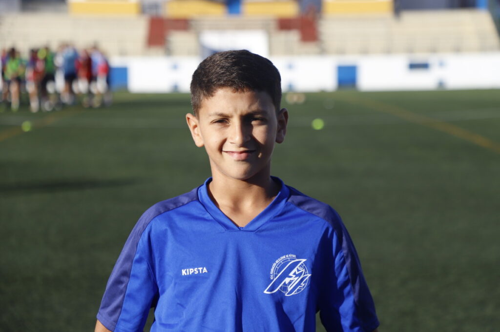 Niño sonriente con camiseta de fútbol en un campo de entrenamiento