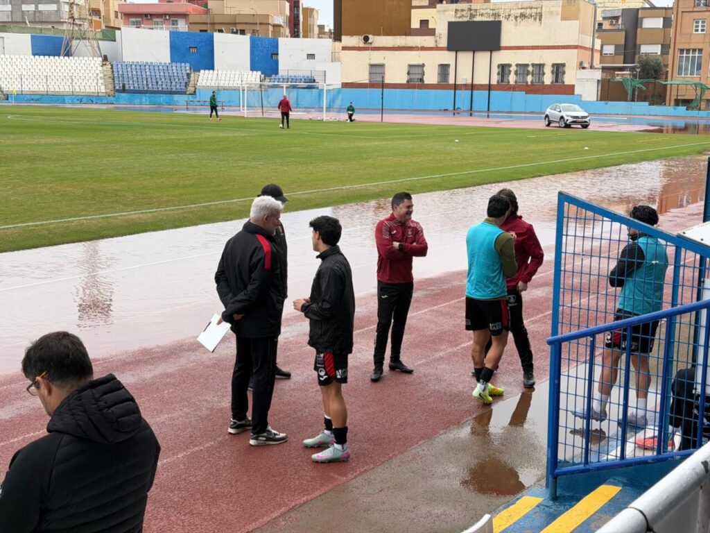Jugadores y cuerpo técnico de la U.D. Melilla en el campo afectado por la lluvia