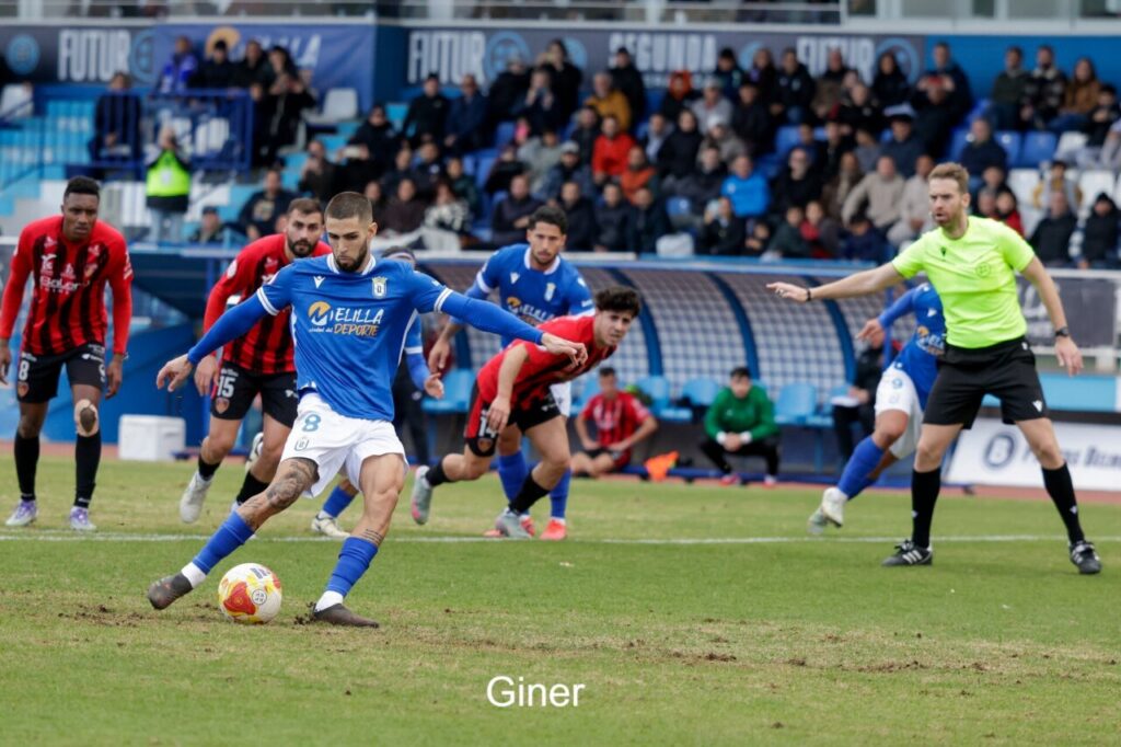 Jugador de la U.D. Melilla ejecutando un penalti durante un partido de fútbol.