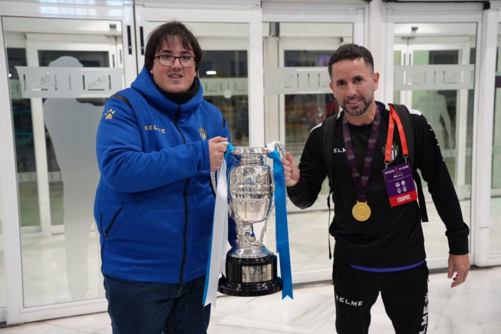 Dos hombres sosteniendo la Supercopa de España en el aeropuerto de Melilla