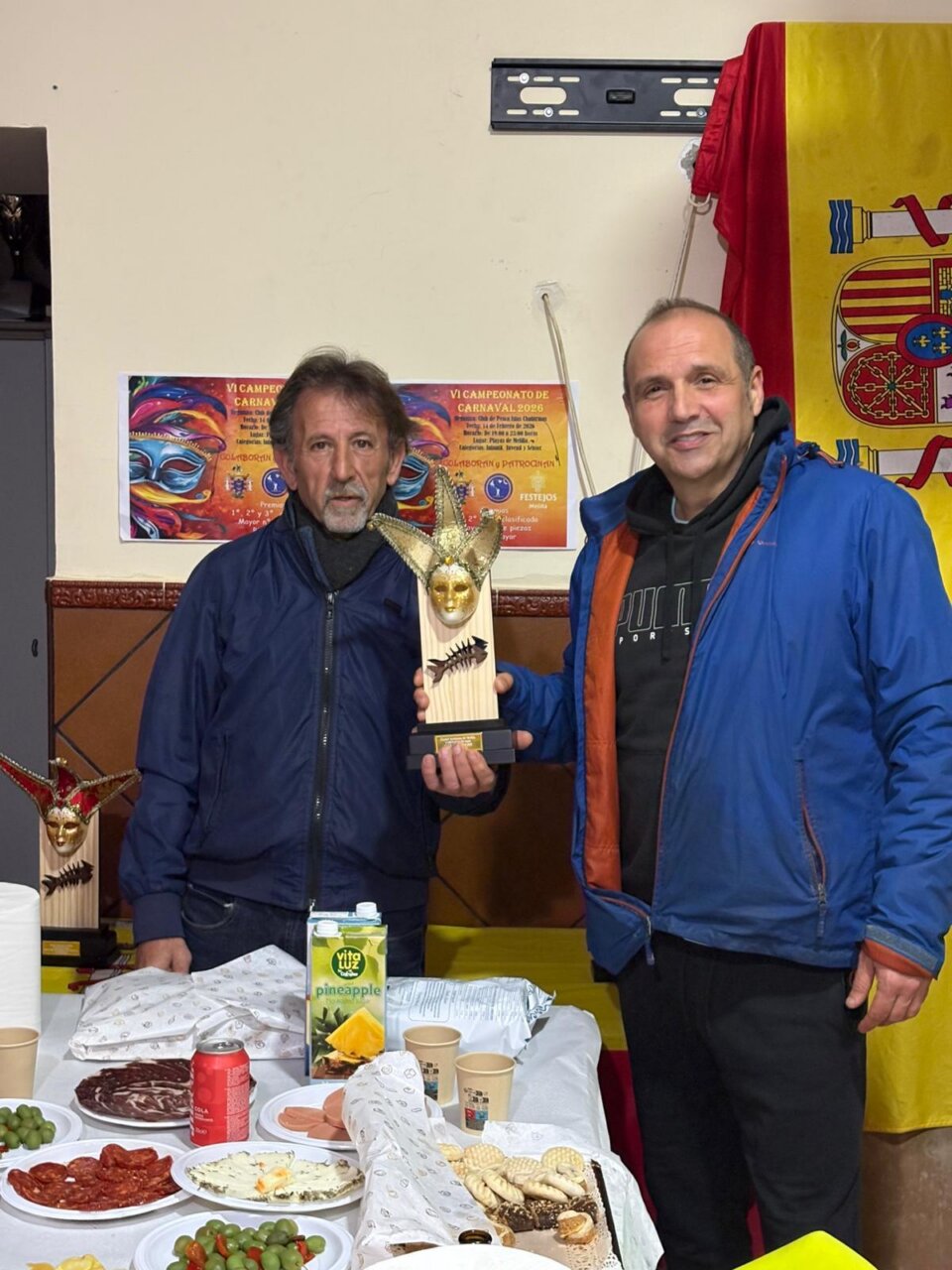 Dos hombres sosteniendo un trofeo en un evento de carnaval